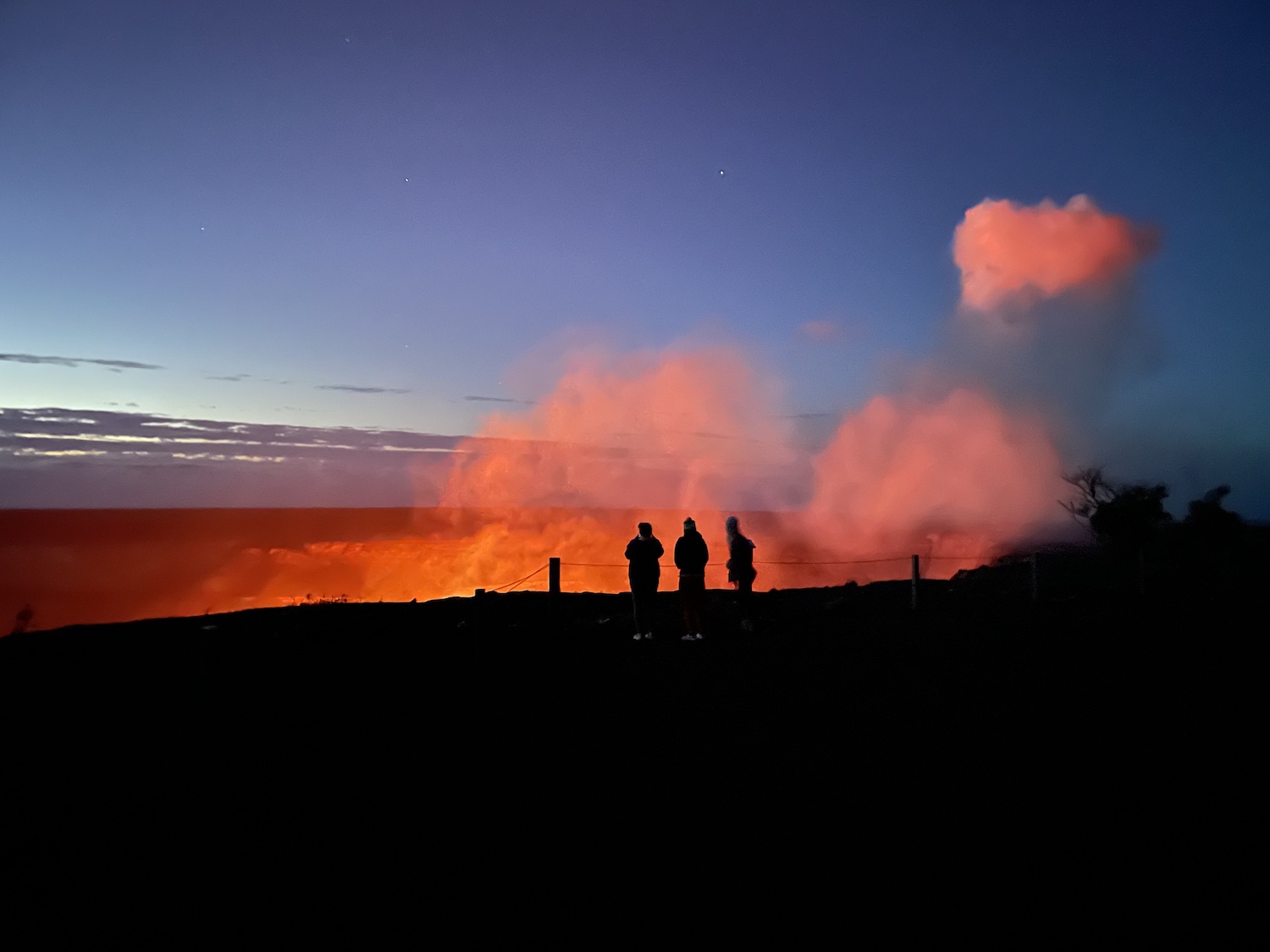 Silhouette of three people with a view of the volcano crater that's glowing from the lava