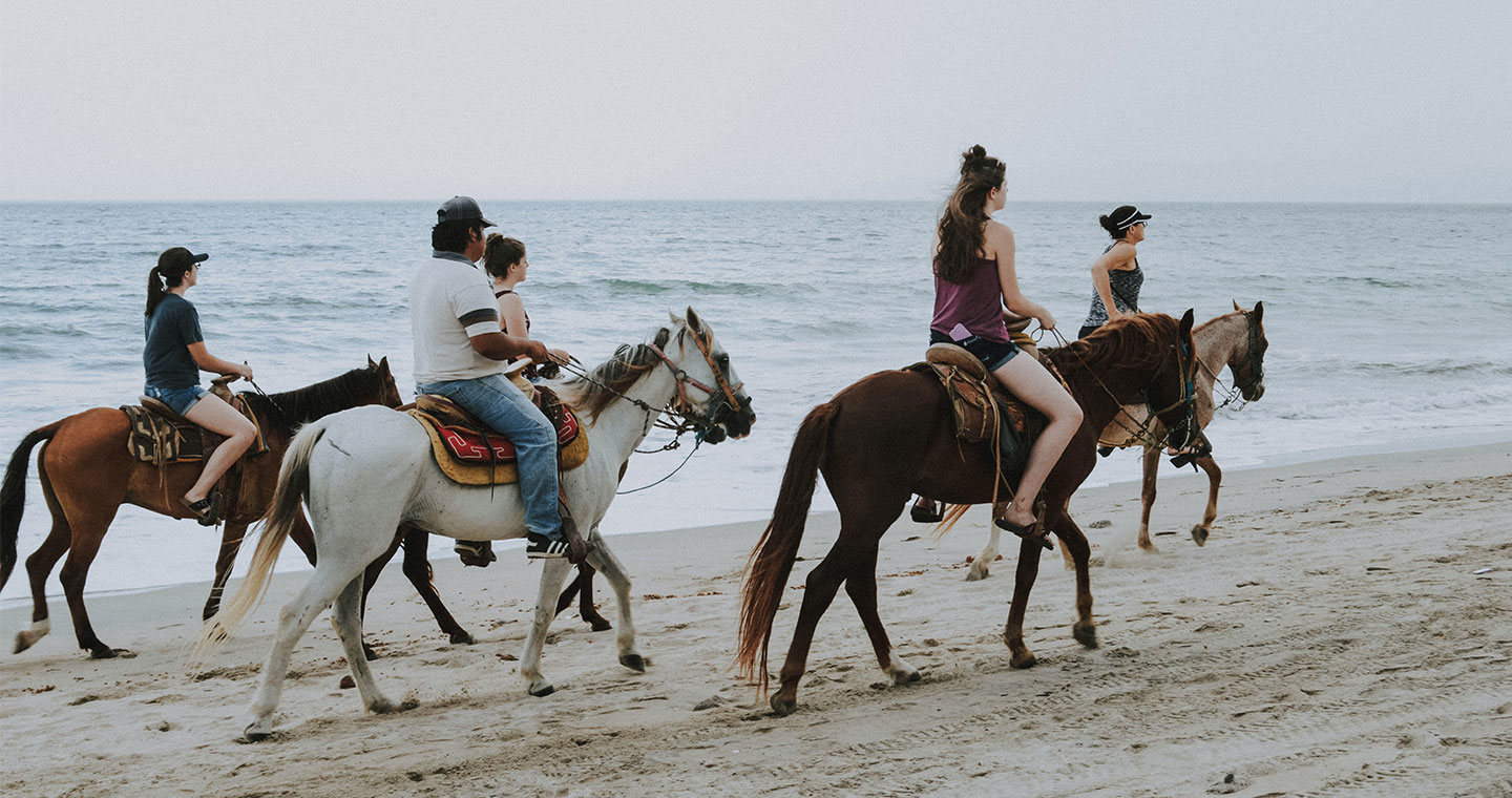 A group of people horseback riding on the shore