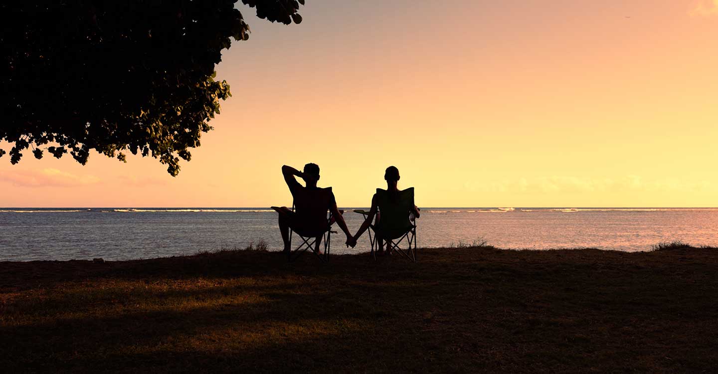 couple sitting on the beach in Hawaii at sunset holding hands