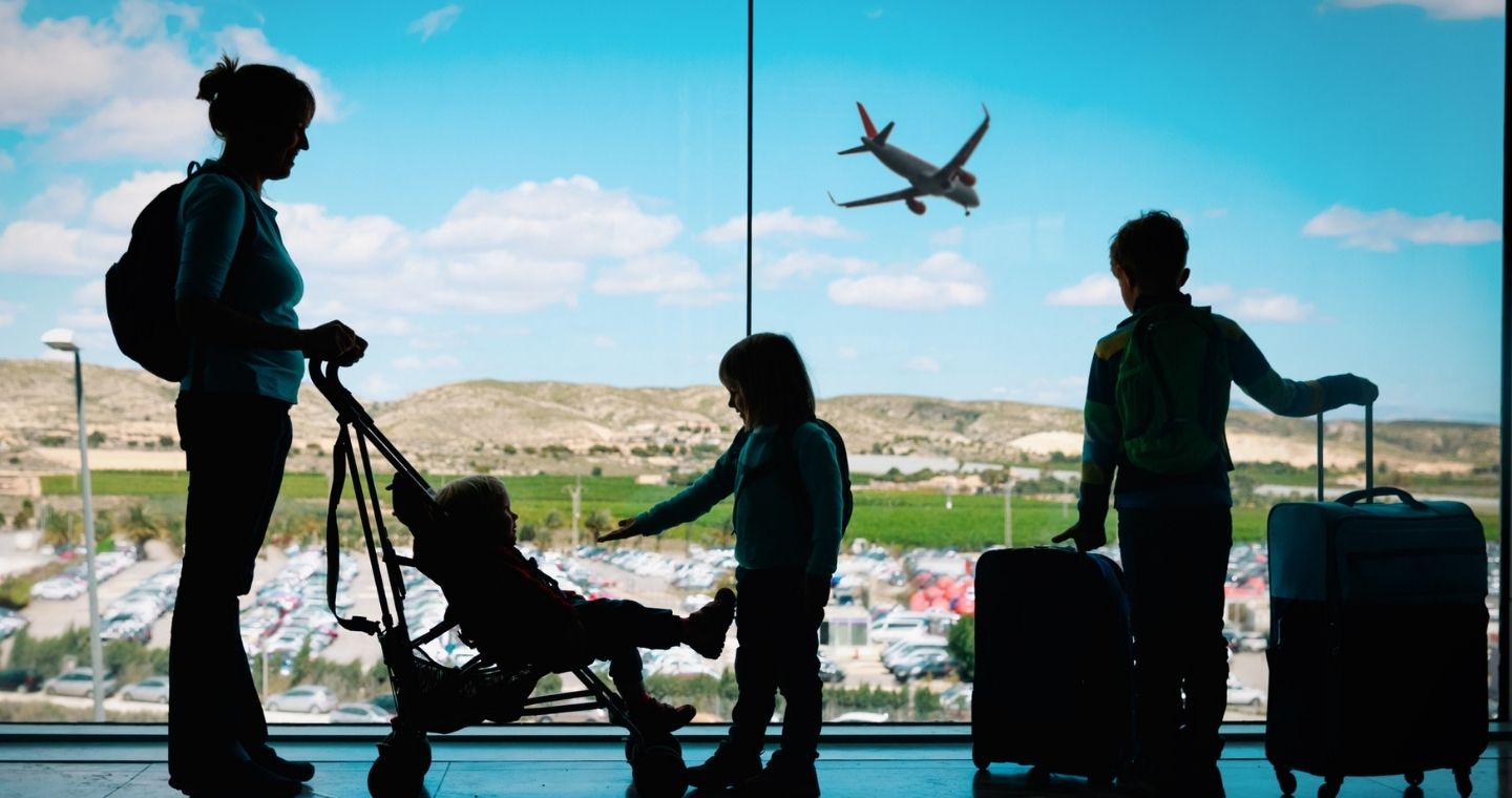 Mother and her three children looking out the window of an airport asa plane goes by