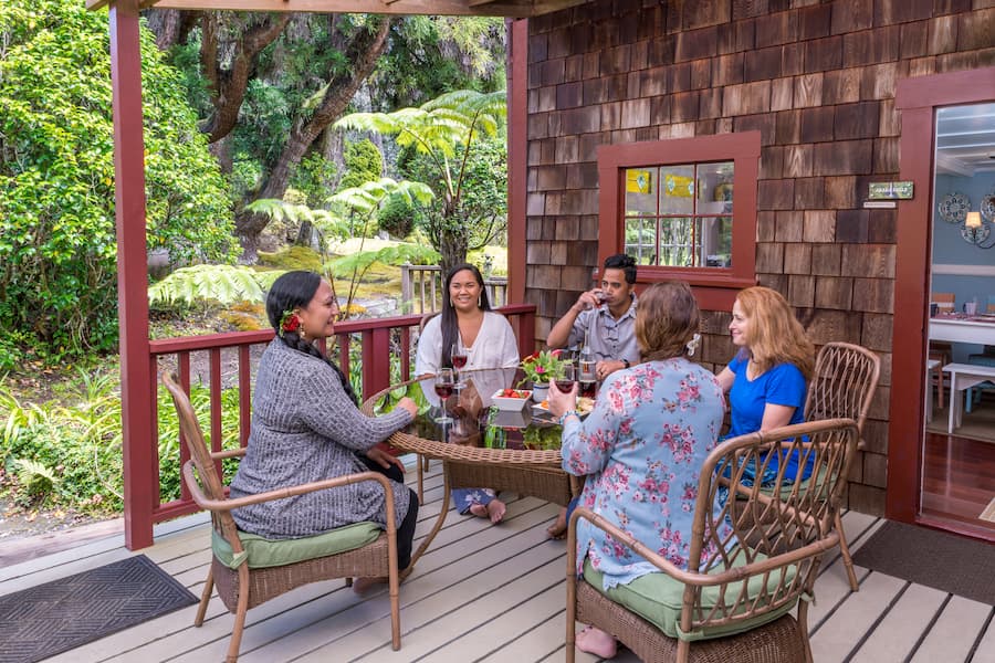 A group of travelers sits around a patio table sipping wine on the lanai at Akaka Falls, a cottage at our Big Island Bed and Breakfast