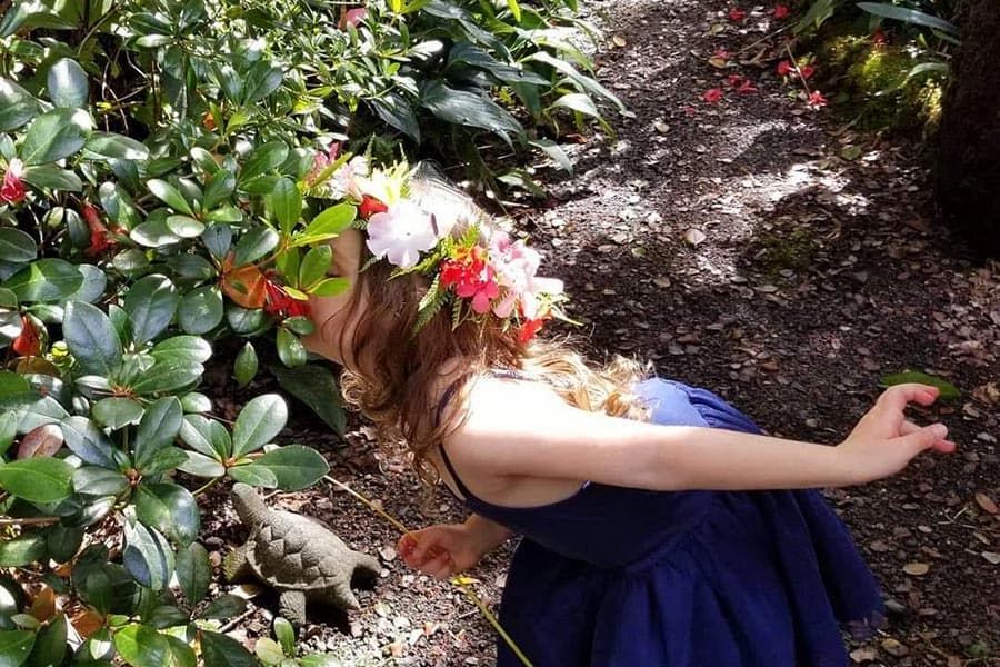 A young girl wearing a flower Haku (Head Lei) stops to smell the flowers on the grounds of our Big Island bed and breakfast