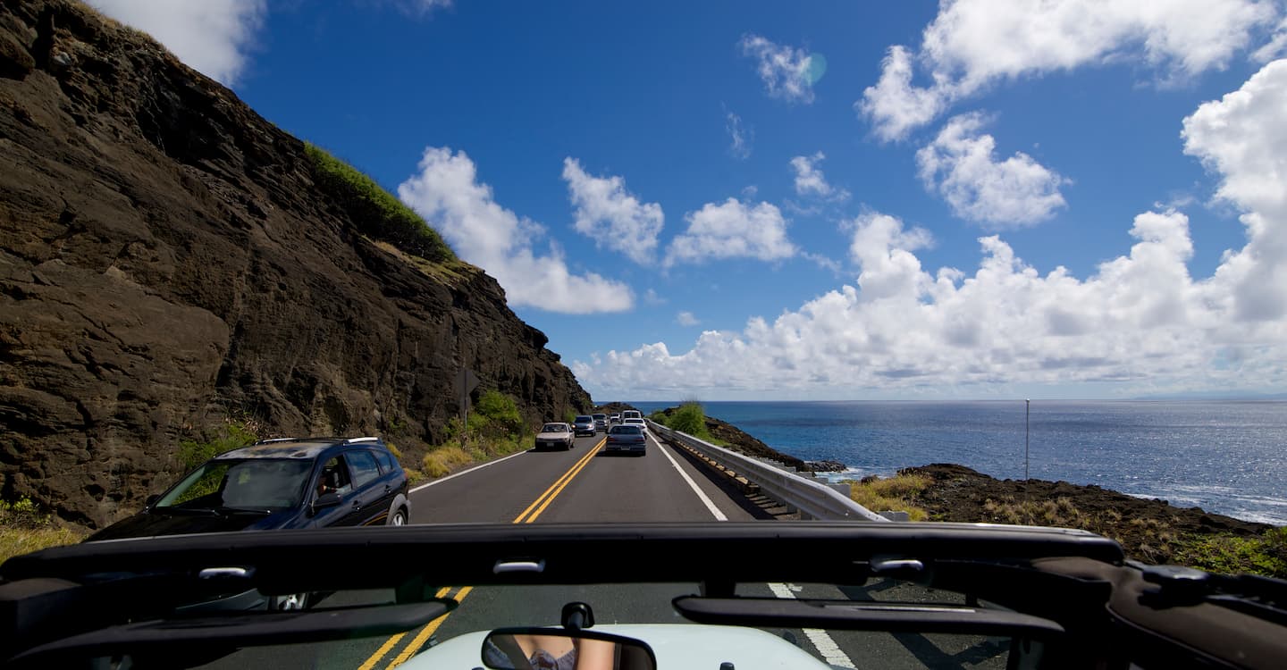The front of a Jeep vehicle from the driver's point of you driving down a scenic highway in Hawaii