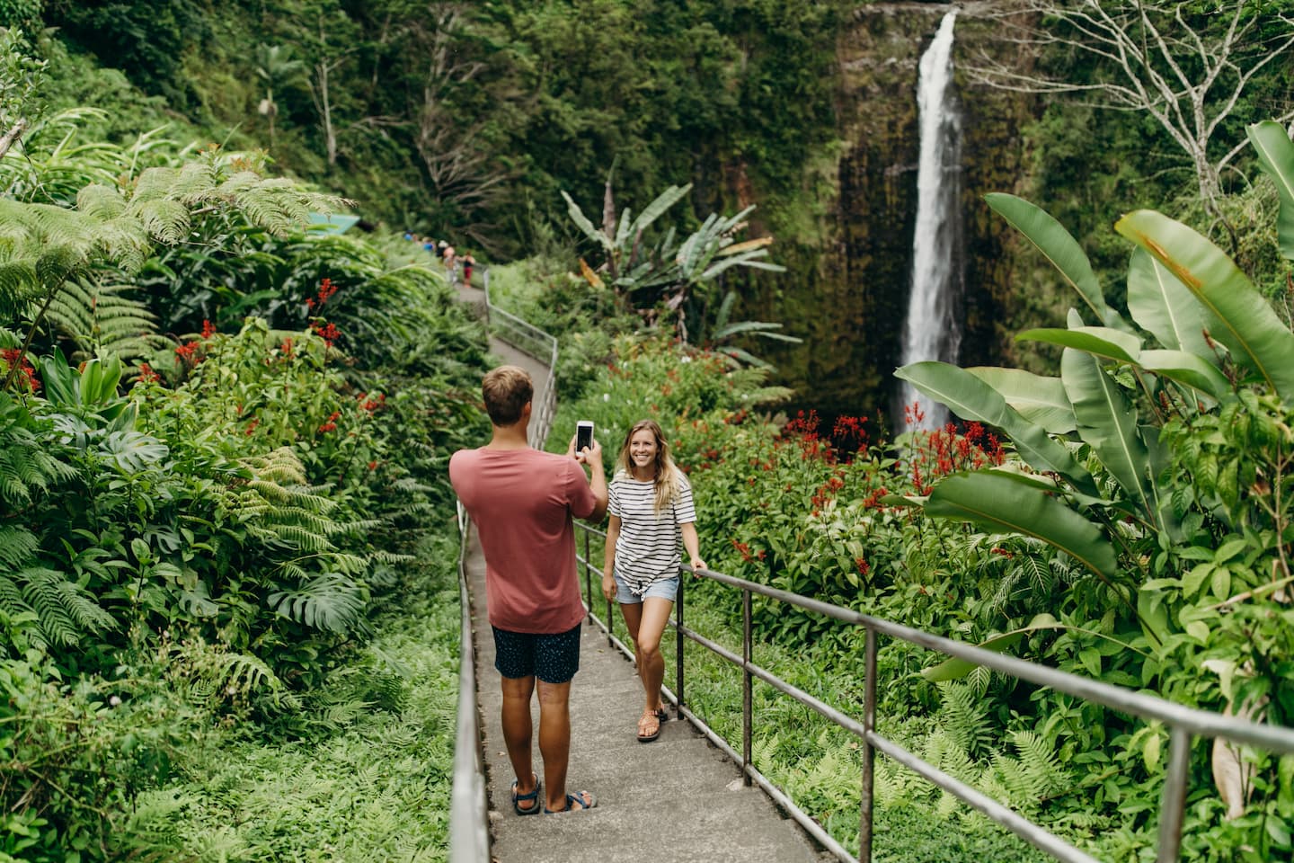 A man taking a picture of his girlfriend in front of the Akaka Falls waterfall on the Big Island